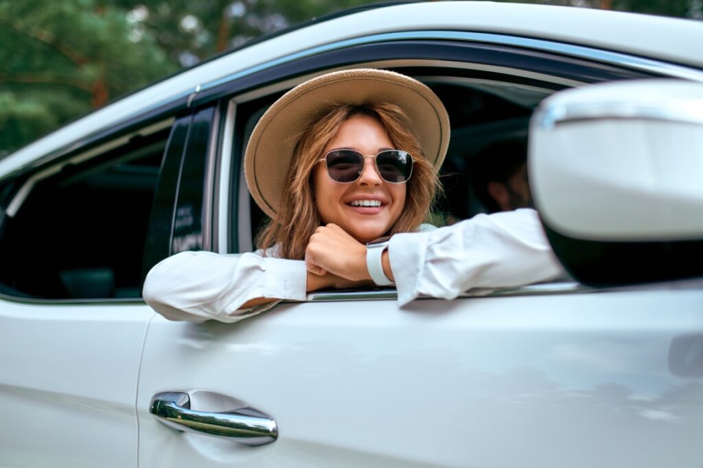 A woman in a hat and sunglasses looks out of the car window and relaxes. Buying a car. Travel, tourism, recreation.